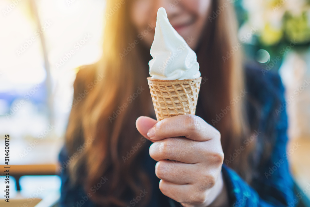 Closeup image of a woman holding and eating soft serve ice cream waffle cone - obrazy, fototapety, plakaty 