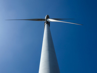 At bottom of tall wind turbine tower with spinning blades under clear blue sky