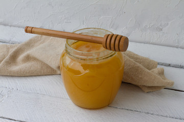 Yellow honey in a glass jar with a wooden spoon. sweet honey on a white wooden background. honey is lying on a white table. space for text. health food. organic food. beekeeper. natural sweets.