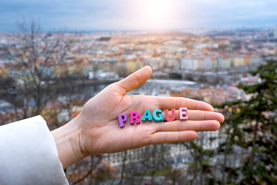 the word Prague of colored letters on the palm of a tourist on the background of the city of Prague in the Czech Republic