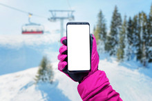 Phone In Girl Hand With Glove On A Ski Lift. Isolated Screen For Mockup. Ski Lift, Resort And Slopes In Background