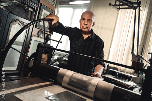 Cuadros en Lienzo Man working on lithography machine looking camera serious balck and white photo