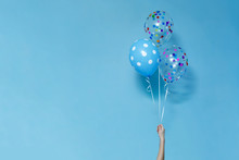 Stylish Birthday Party Or Holidays With Balloons Close Up. Blue  Balloons Isolated  On The Blue Background With Copy Space For Text. Hand  Holding Three Bright Colorful Balloons Indoor.