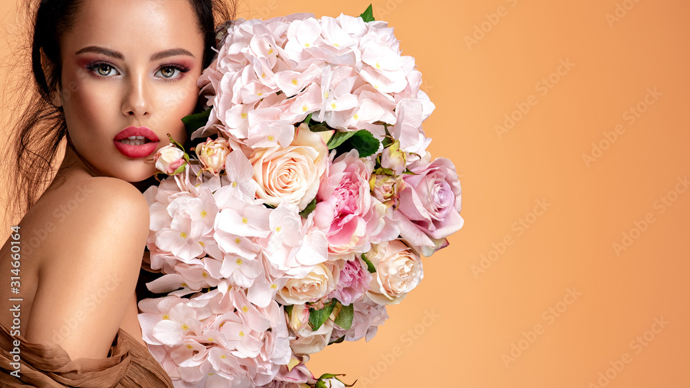 Beautiful white girl with flowers. Stunning brunette girl with big bouquet flowers of roses. Closeup face of young beautiful woman with a healthy clean skin. Pretty woman with bright makeup - obrazy, fototapety, plakaty 
