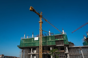 Cranes and building construction site against blue sky. Metal construction of unfinished building on construction. Tower Crane use for building of multi storage building.