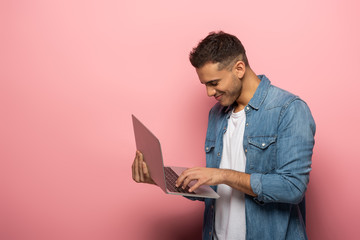 Side view of smiling man using laptop on pink background