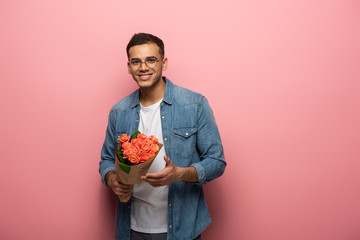 Young man with rose flowers smiling at camera on pink background