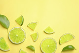 Juicy fresh lime slices and green leaves on yellow background, flat lay. Space for text