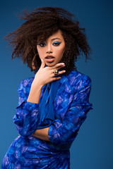 stylish african american woman with makeup in dress looking at camera isolated on blue