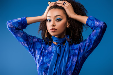 stylish african american woman in dress looking at camera isolated on blue