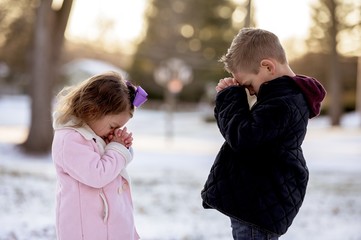 Selective focus shot of cute little kids praying in the middle of a winter park