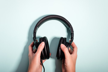 Black massive headphones in female hand on pastel background, copy space. Modern technology flat lay with over-ear earphones in woman hand, modern lifestyle concept