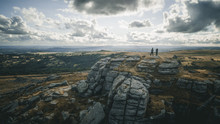 A Drone Shot Of Two People Standing On The Rocky Hill In Dartmoor Country Park
