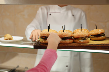 Little girl taking burger at serving line in canteen. School food