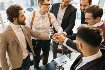 Wall Mural - young caucasian colleagues joined hands in one, wearing formal suits, successful cooperation of confident business people. success depends on cohesion and teamwork