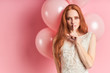 Beautiful flirty woman with auburn hair stand in coquettish gesture. Pink air balloons behind.Pink isolated background