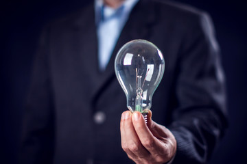 Businessman in suit holding bulb in hand in front of black background