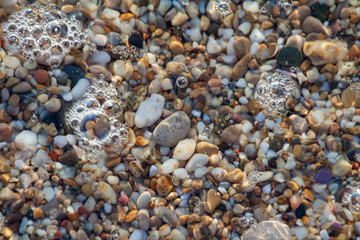 sea pebbles colored granite on the beach background stones. The shore of the beach with sand and pebbles washed by the waves of the sea.