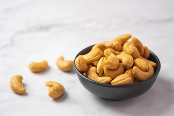 Top view of roasted cashew nut in salt in black bowl on white marble floor