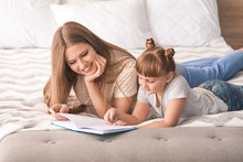 Beautiful Young Woman And Her Little Daughter Reading Book At Home