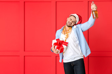 Sticker - Drunk man with Santa Claus hat, gift and champagne on color background