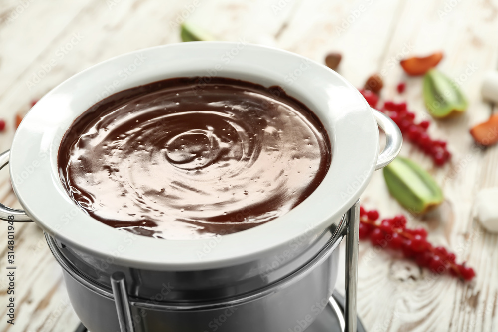 Fondue pot with melted chocolate on table, closeup