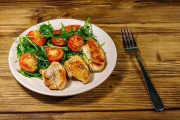 Fried chicken breast with salad of fresh arugula and cherry tomatoes on wooden table