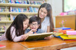 © Songkhla Studio - A Group of Asian Student Kid Reading a book with women teacher in School library with Shelf of Books in Background, Asian Kid Education Concept