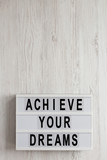 Fototapeta  - 'Achieve your dreams' words on a modern board on a white wooden background, top view. Overhead, from above, flat lay. Copy space.