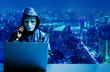 © TeTe Song - Anonymous computer hacker in white mask and hoodie. Obscured dark face using laptop computer for cyber attack and calling on cellphone  on modern city background, Data thief, internet attack.