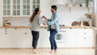 © fizkes - Happy family couple dancing barefoot on wooden floor in kitchen.