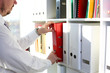 © H_Ko - Male arms pick red file folder from office book shelf closeup. Store pile of project documentation concept