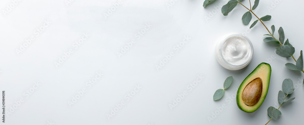 Cosmetic jar of facial cream with fresh avocado on white table - obrazy, fototapety, plakaty 