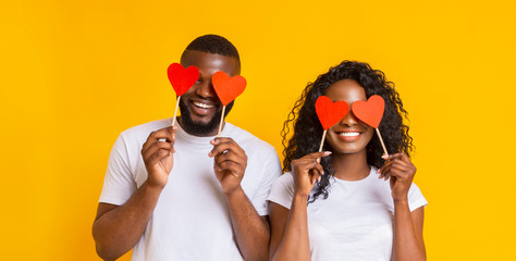 Wall Mural - Cheerful black couple covering eyes with red heart paper cards