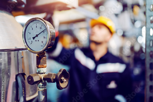 Close up of clock on boiler showing pressure on boiler. In background is worker working. Selective focus on clock.