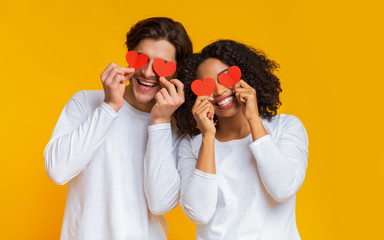 Wall Mural - Romantic interracial couple holding red hearts over eyes and smiling