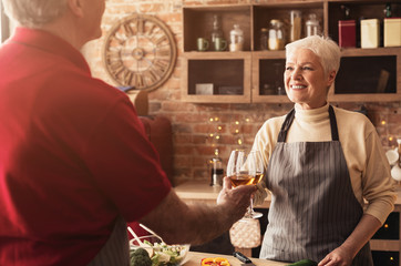 Wall Mural - Aged couple in love clinking with wine glasses at kitchen