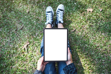 Top view mockup image of a woman holding and using black tablet pc with blank white desktop screen while sitting in the outdoors