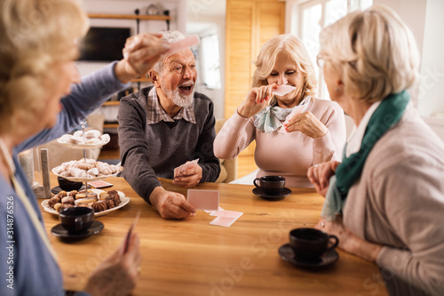 Fotomural Happy mature man playing cards with friends at home.