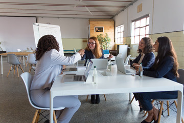 Smiling businesswomen meeting in office. Multiethnic female colleagues sitting around table with laptops and discussing work in office. Women in business concept