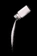 Salt is poured from a salt shaker on a black background. Salt shaker spills salt. A stream of salt.