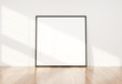 © sdecoret - Black frame leaning in bright white interior with wooden floor mockup 3D rendering