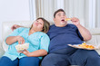 © Creativa Images - Fat Asian couple eating pizza and popcorn drowsily