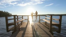 Couple Running On A Wooden Pier And Jumping Into The Lake After The Sauna In Summer White Night In Finland.