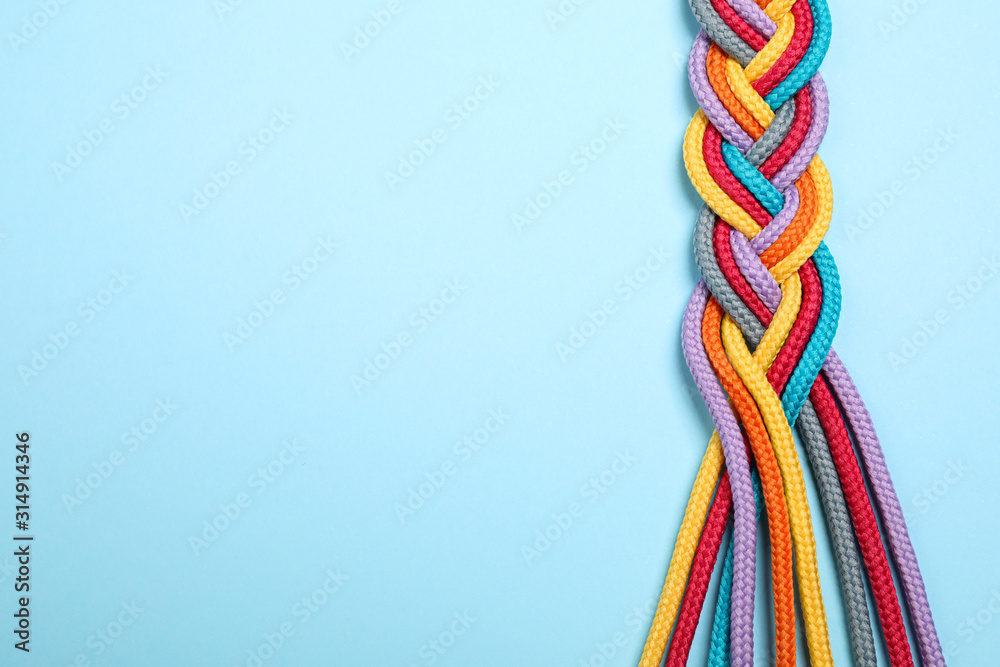 Top view of braided colorful ropes on light blue background, space for text. Unity concept - obrazy, fototapety, plakaty 