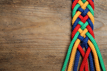 Wall Mural - Top view of braided colorful ropes on wooden background, space for text. Unity concept