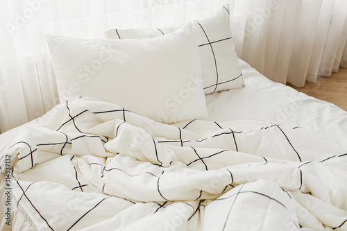 Fotografía White bedding sheets with striped blanket and pillow. Messy bed.