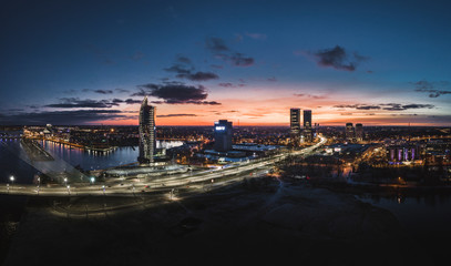 Aerial view over Riga city at night time. Urban landscape with skyscrapers and highway with city lights.