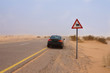 The car in dessert stopped next to sign warning about camels crossing the road