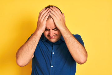 Poster - Young man wearing denim casual shirt standing over isolated yellow background suffering from headache desperate and stressed because pain and migraine. Hands on head.